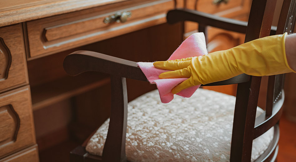 Close up of a person wiping off a wooden chair using a microfiber cloth