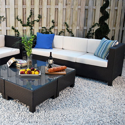 Black wicker sofa with white cushions with a matching coffee table sitting in a gravel space