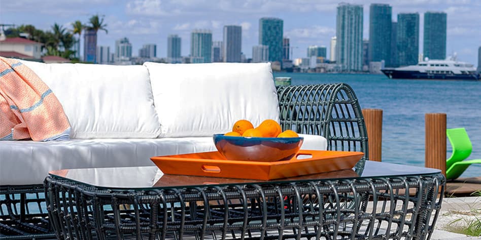 mobilier d'extérieur noir avec coussins blancs sur une terrasse au bord de l'eau avec un paysage urbain en arrière-plan