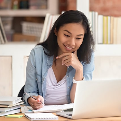 Mujer joven usando una computadora y tomando notas