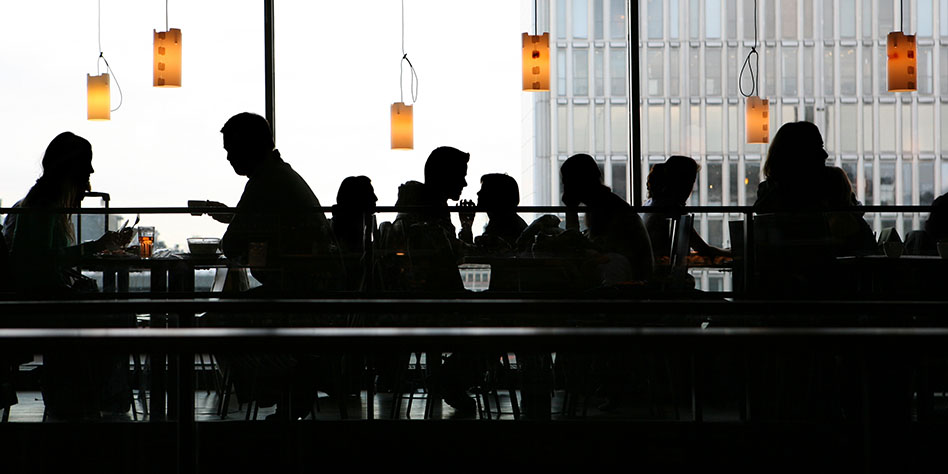 Silueta de personas que se reúnen y comen en un restaurante urbano moderno.