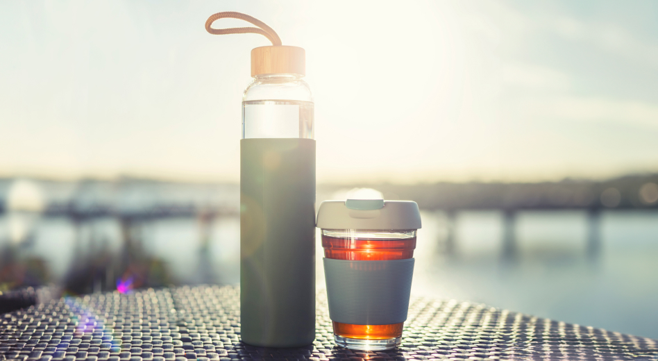 Botella de agua de vidrio y taza de café de viaje en el patio al aire libre del resort