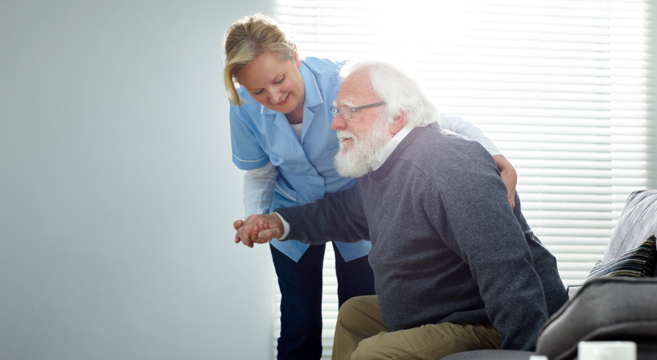 Caretaker helps elderly man stand up from a couch